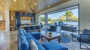 Ein modernes Wohnzimmer mit Holzboden, einer großen Couch, einem Esstisch und Blick auf ein Gewässer.