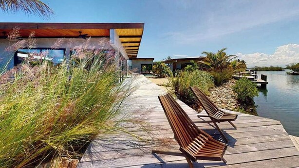 A waterfront property with a wooden deck, benches, and a building with a modern design. - Elegant waterfront villa with private terrace, pool, beach access & 4 en-suites (Placencia)