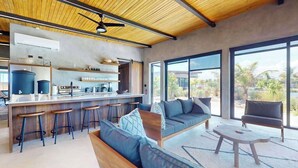 A modern kitchen with bar stools, a sofa, and a coffee table. - Elegant waterfront villa with private terrace, pool, beach access & 4 en-suites (Placencia)