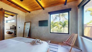 A bedroom with a bed, a window with a view of palm trees, a wooden ceiling, and a chair. - Elegant waterfront villa with private terrace, pool, beach access & 4 en-suites (Placencia)