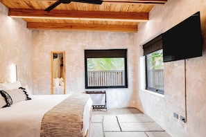 A bedroom with a bed, a window with a view of greenery, a television mounted on the wall, and a wooden ceiling. - Modern Waterfront Villa | Private Pool & Dock (Placencia)