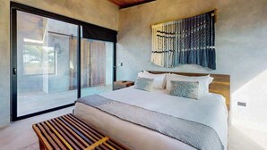 A bedroom with a large bed, a wooden bench, a wall-mounted tapestry, and a sliding glass door. - Elegant waterfront villa with private pool, terrace and beach club access (Placencia)