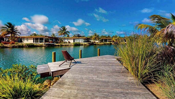 A wooden dock leading to a calm body of water, with a chair on the dock and a row of buildings in the background. - Elegant waterfront villa with private pool, terrace and beach club access (Placencia)