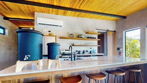 A modern kitchen with a central island, bar stools, and a view of the outdoors. - Elegant waterfront villa with private pool, terrace and beach club access (Placencia)