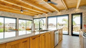 A modern kitchen with wooden cabinets, a large island, and a view of the outdoors. - Tranquil waterfront villa with private deck & full kitchen (Placencia)
