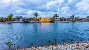 A hotel with a pool, palm trees, and a cloudy sky. - Tranquil waterfront villa with private deck & full kitchen (Placencia)