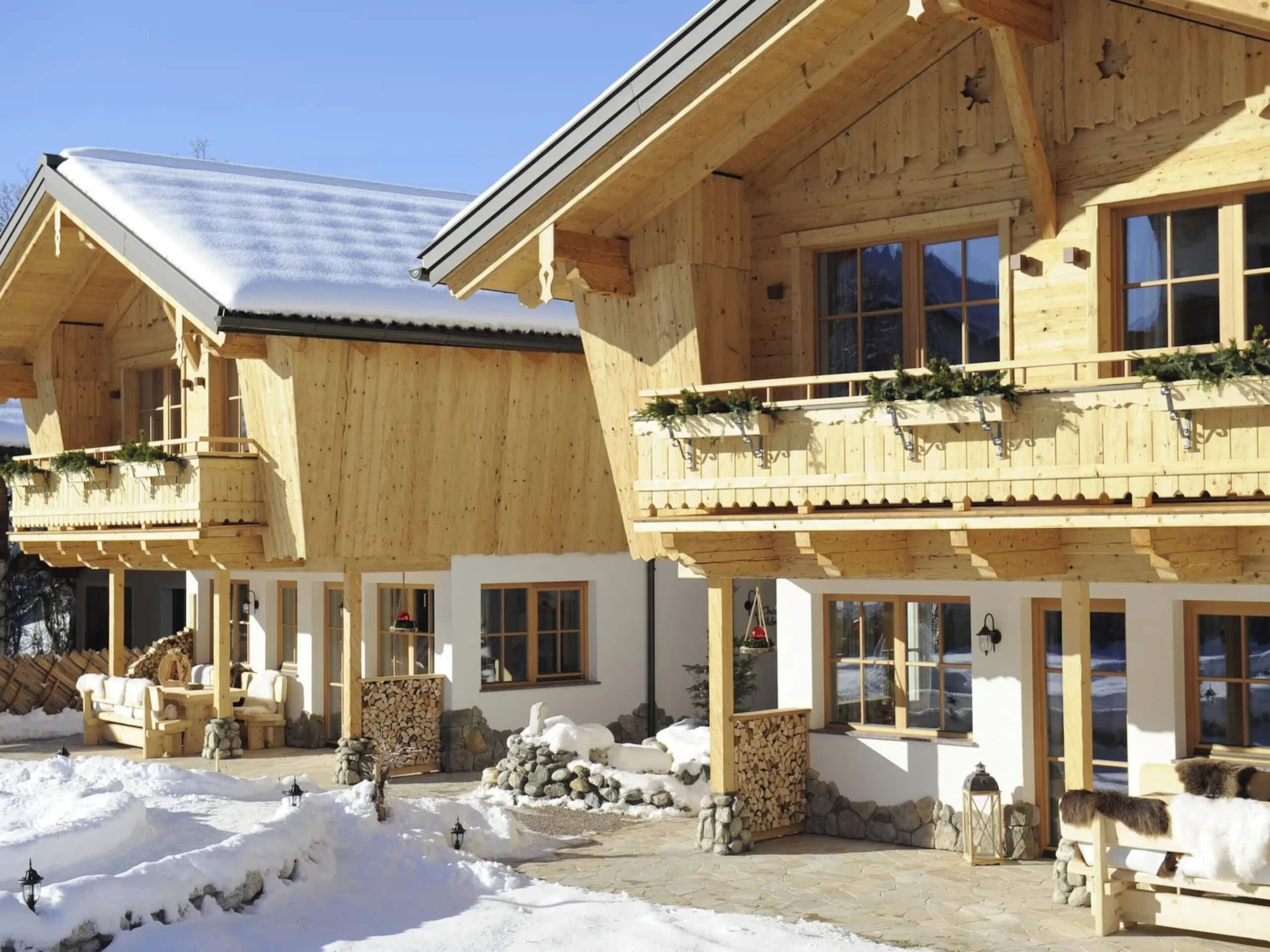 Eine Holzhütte mit Balkonen, Steinmauern und einem mit Schnee bedeckten Gelände.