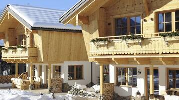 Eine Holzhütte mit Balkonen, Steinmauern und einem mit Schnee bedeckten Gelände.