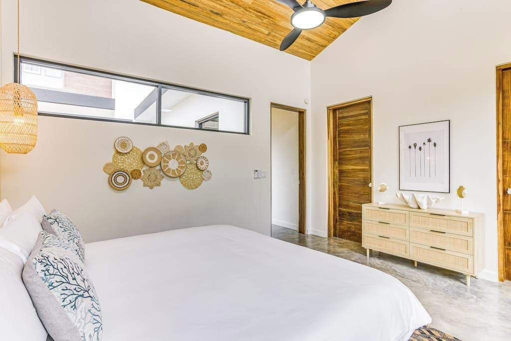 A bedroom with a large bed, a ceiling fan, a dresser, and a wall with decorative items.