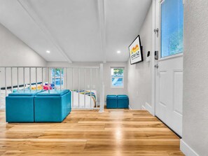 A spacious room with a wooden floor, a large blue sofa, a bed with colorful bedding, and a window with a view of a pool. - The Poolside Club - Pool/Spa/Swim Up Bar (Phoenix)