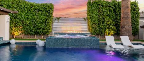 A swimming pool with a hot tub, lounge chairs, and a sunset view.