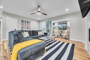 A modern living room with a sectional sofa, a coffee table, a striped rug, a ceiling fan, and a large window. - The Poolside Club - Pool/Spa/Swim Up Bar (Phoenix)