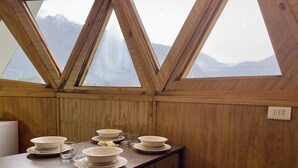 A dining area with a table set for four, wooden walls, and a view of mountains through triangular windows.