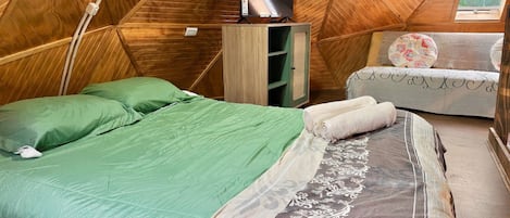 Una habitación acogedora de estilo tienda de madera triangular con cama, televisión y sofá.