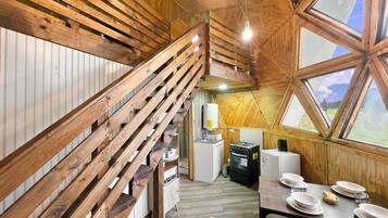Un interior de madera con una escalera, una mesa de comedor dispuesta con platos y vistas a través de un ventanal.