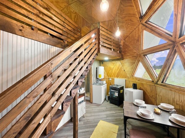 A wooden interior with a staircase, a dining table set with plates, and a view through a large window.