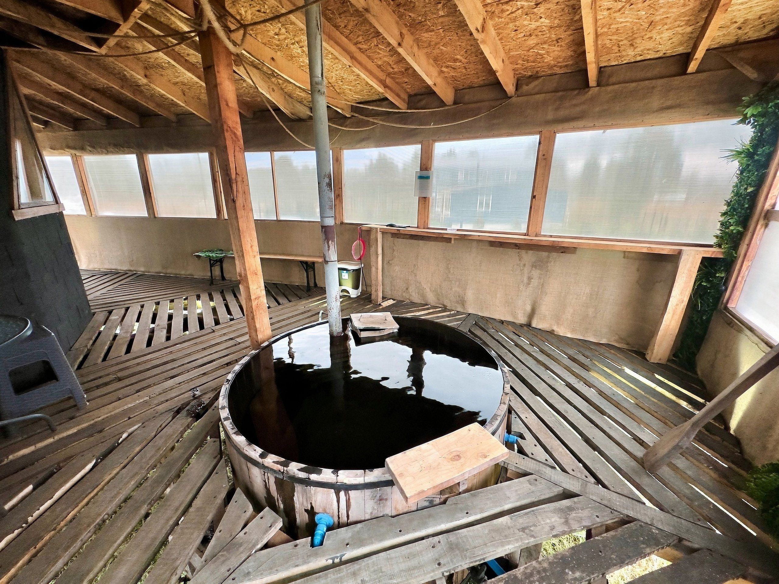 Eine Holzterrasse mit einem zentralen Wasserspiel, hölzernen Bänken und Blick durch große Fenster.