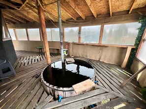 Eine Holzterrasse mit einem zentralen Wasserspiel, hölzernen Bänken und Blick durch große Fenster.