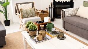 Ein Wohnzimmer mit einem weißen Couchtisch, einem Kamin, einem grauen Sofa und einem großen Wandteppich.