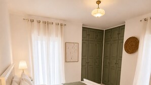Ein Schlafzimmer mit einem Bett, einem Nachttisch, einer Lampe, einem grünen Kleiderschrank und einem an der Wand befestigten Kunstwerk.