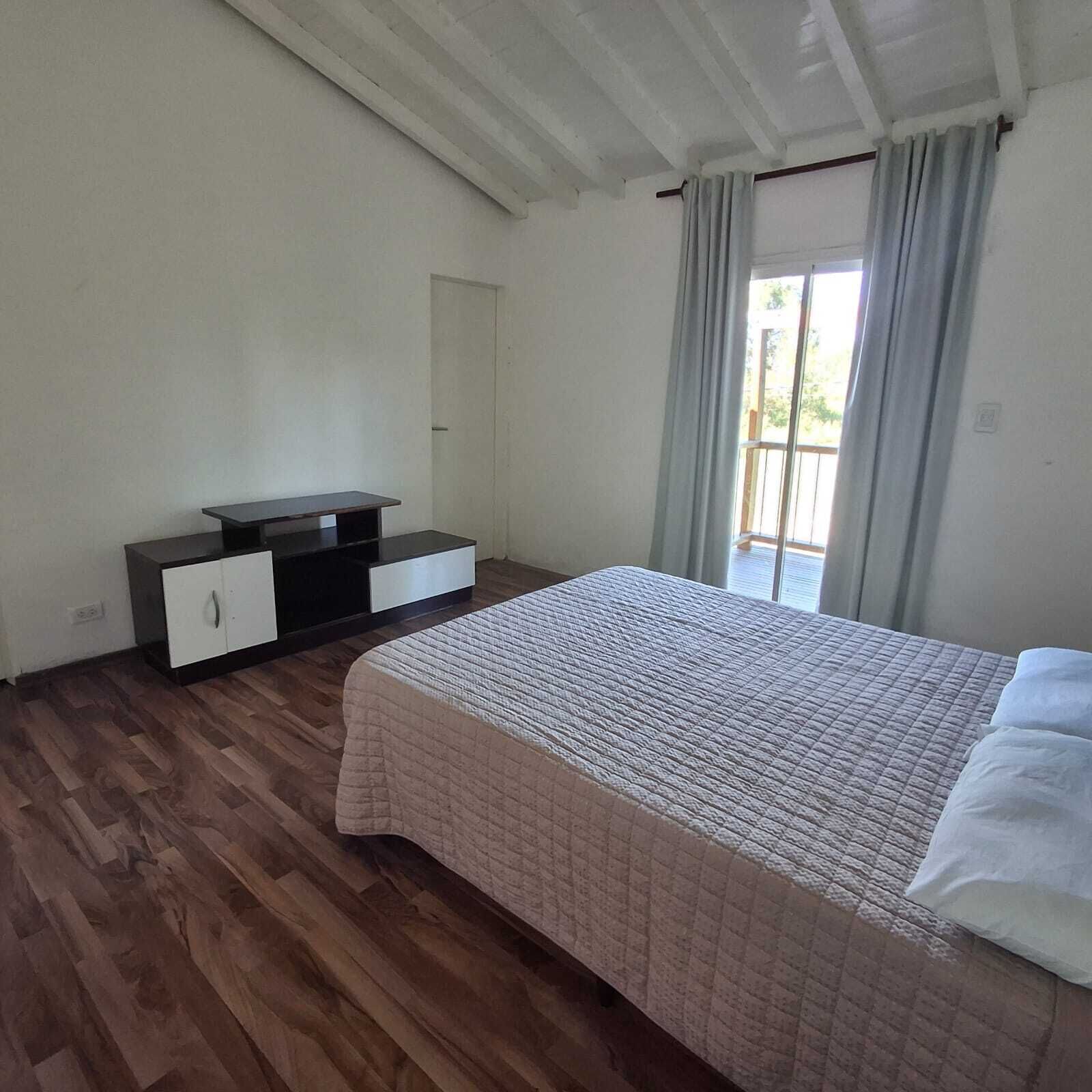 A bedroom with a bed, a dresser, a window with curtains, and a door.