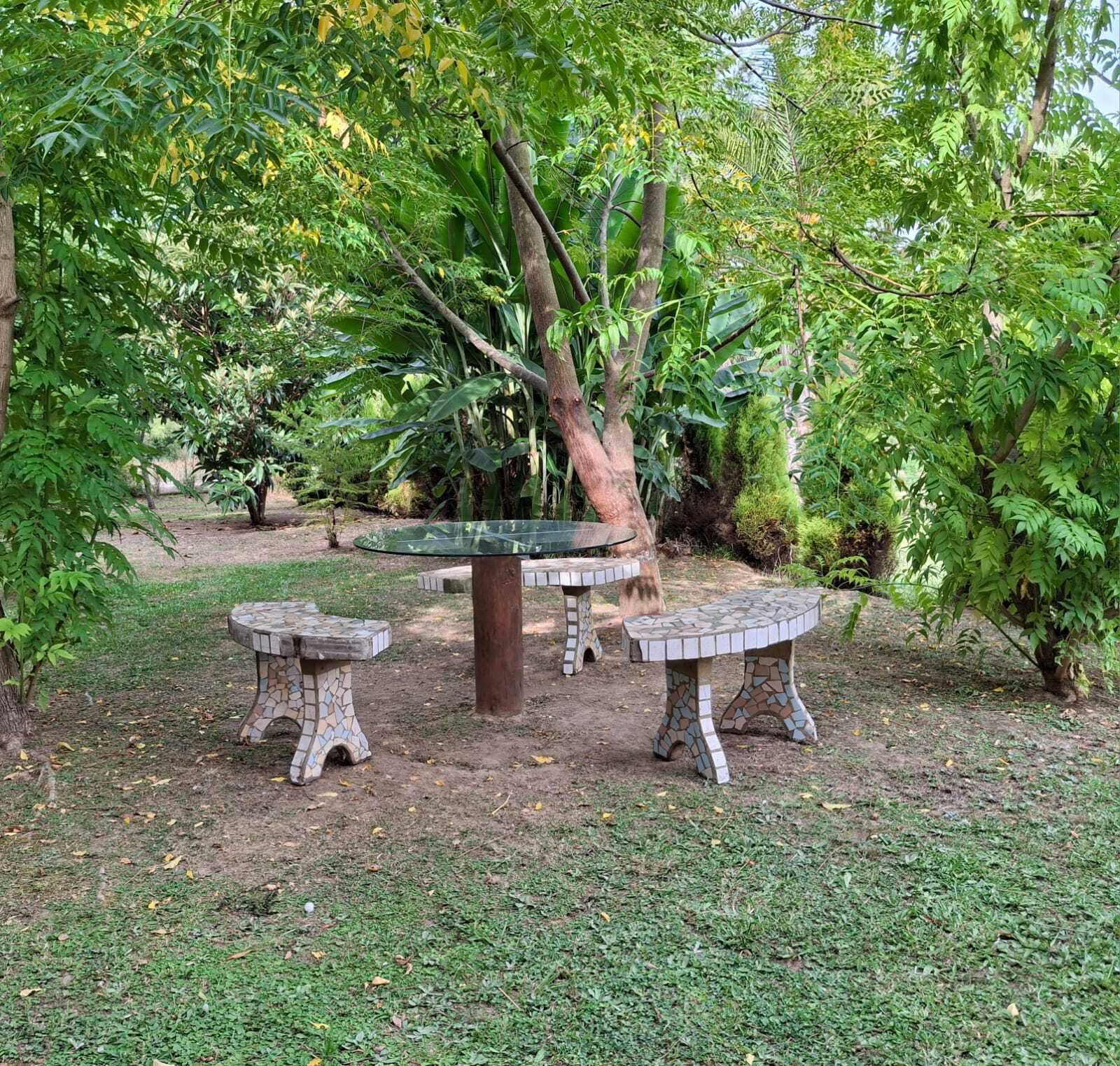 Un jardin avec une table centrale ornée de mosaïques, entourée de trois bancs également décorés de mosaïques.