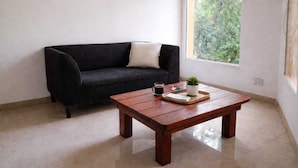 Una habitación con un sofá negro, una mesa de centro de madera con una planta, una taza y una bandeja.
