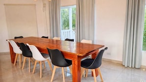 Un comedor con mesa y sillas de madera, ventanas grandes con cortinas y vistas a la vegetación exterior.