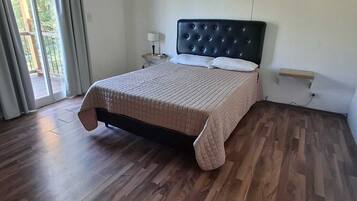 Un dormitorio con cama, suelo de madera, ventana con cortinas y aire acondicionado.
