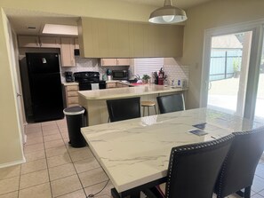 Une cuisine dotée d’un plan de travail en marbre, de chaises noires, d’un réfrigérateur noir et d’une fenêtre avec des stores.