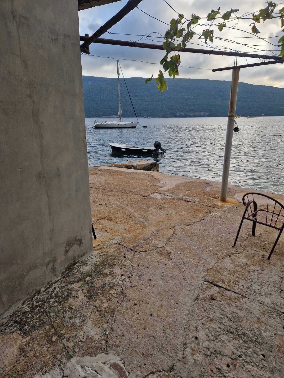 Eine Betonkonstruktion mit einem Metallstuhl, einem Steg mit einem Boot und einem Segelboot im Hintergrund.