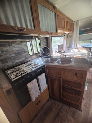 Cocina compacta para autocaravana con estufa a gas, lavamanos y armarios de madera.