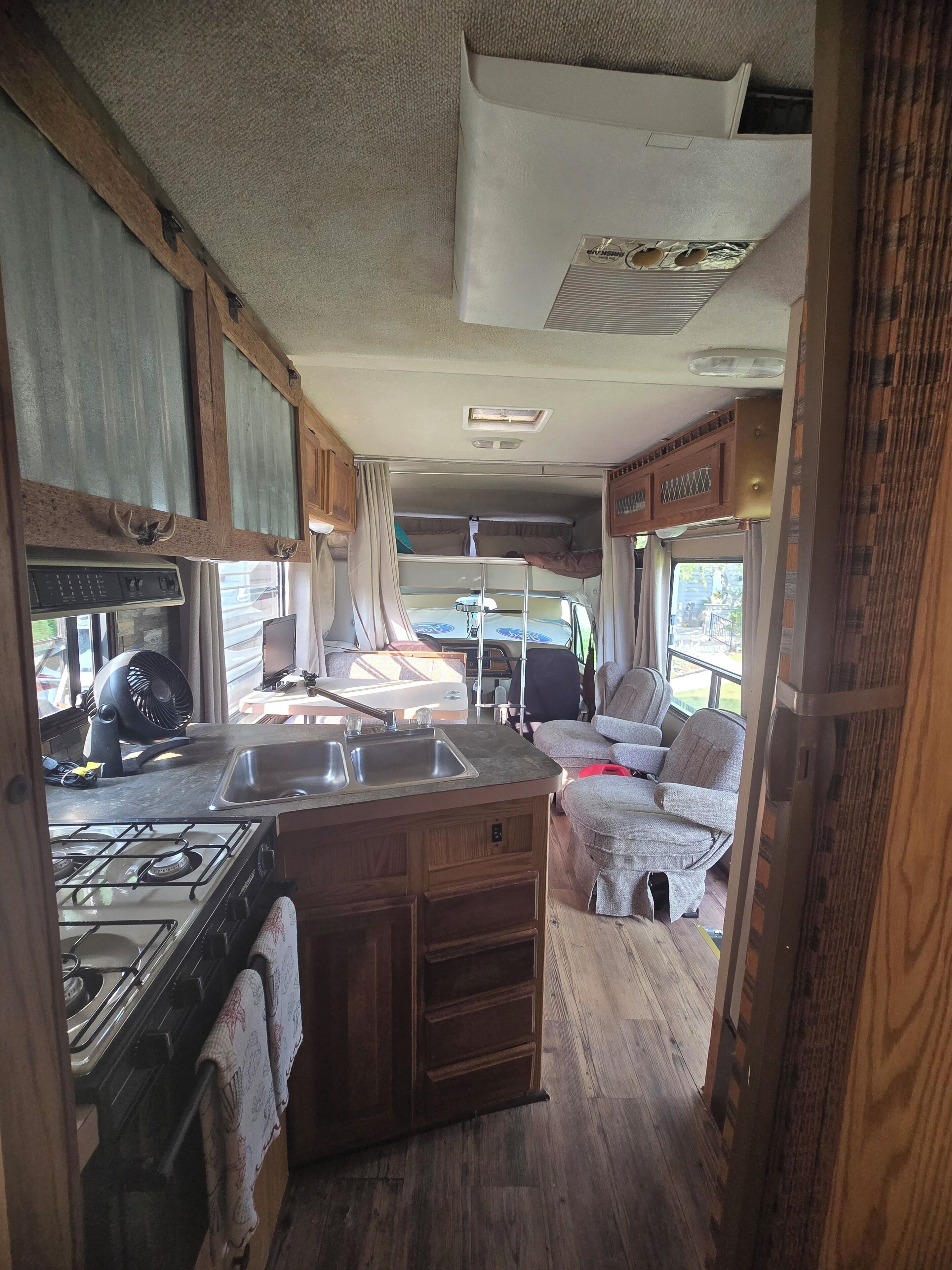 A compact RV kitchen with a stove, sink, and wooden cabinetry.