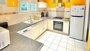 Eine Küche mit Holzboden, gelben Wänden, weißen Schränken, einem Spülbecken, Herd, Backofen und Kühlschrank.