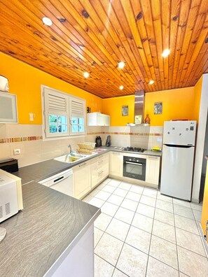 A kitchen with wooden ceiling, yellow walls, white cabinets, a sink, stove, oven, and a refrigerator. - Villa Solana, private pool with tropical garden in Sainte-Luce (Sainte-Luce)