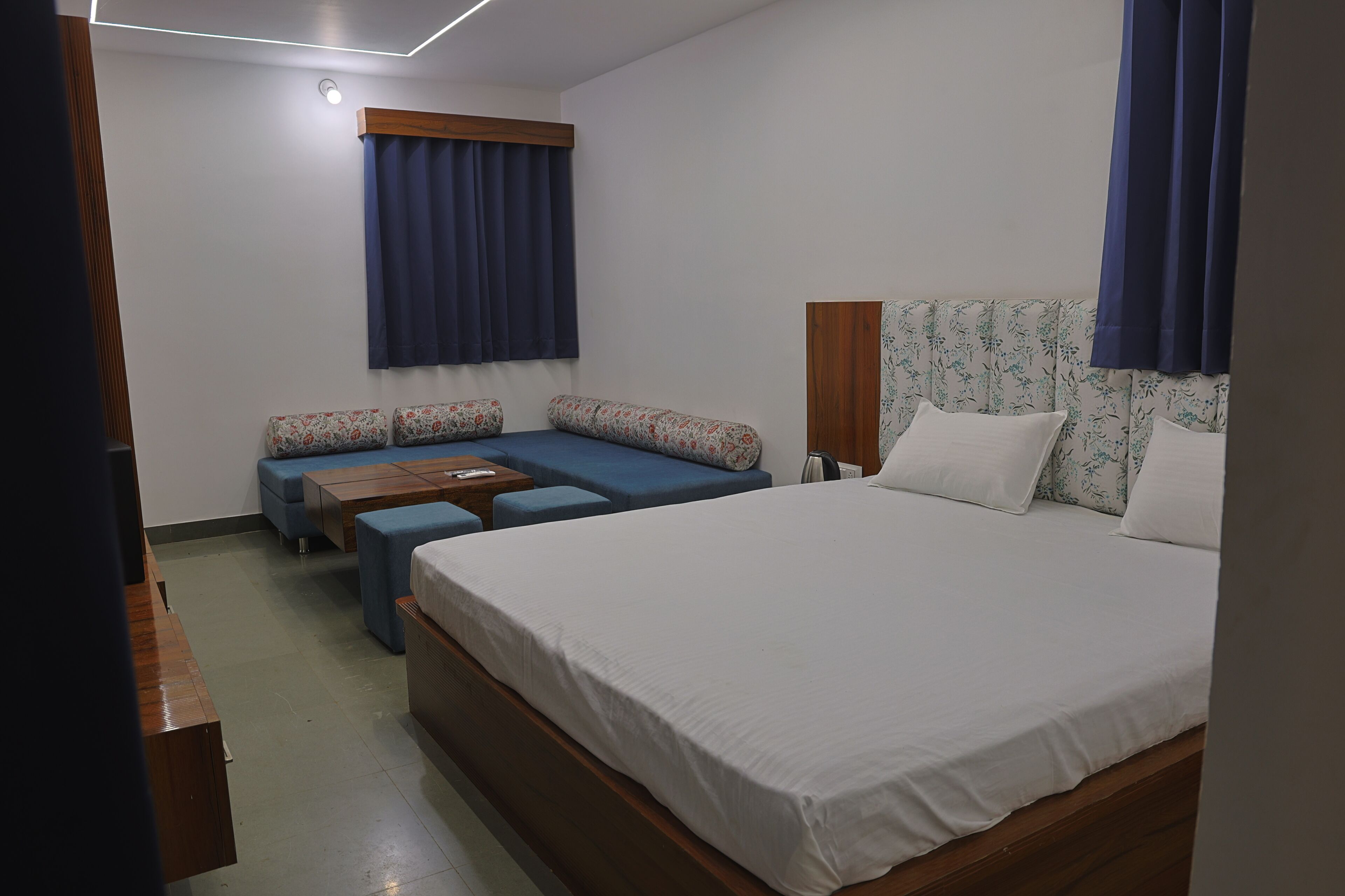 A hotel room with a bed, a sofa, a small table, and a window with curtains.