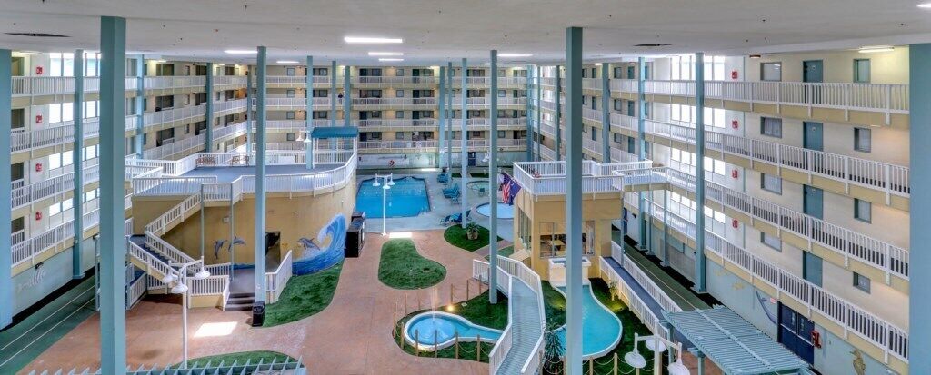 A multi-level hotel atrium with a central swimming pool, multiple balconies, and a children's play area.
