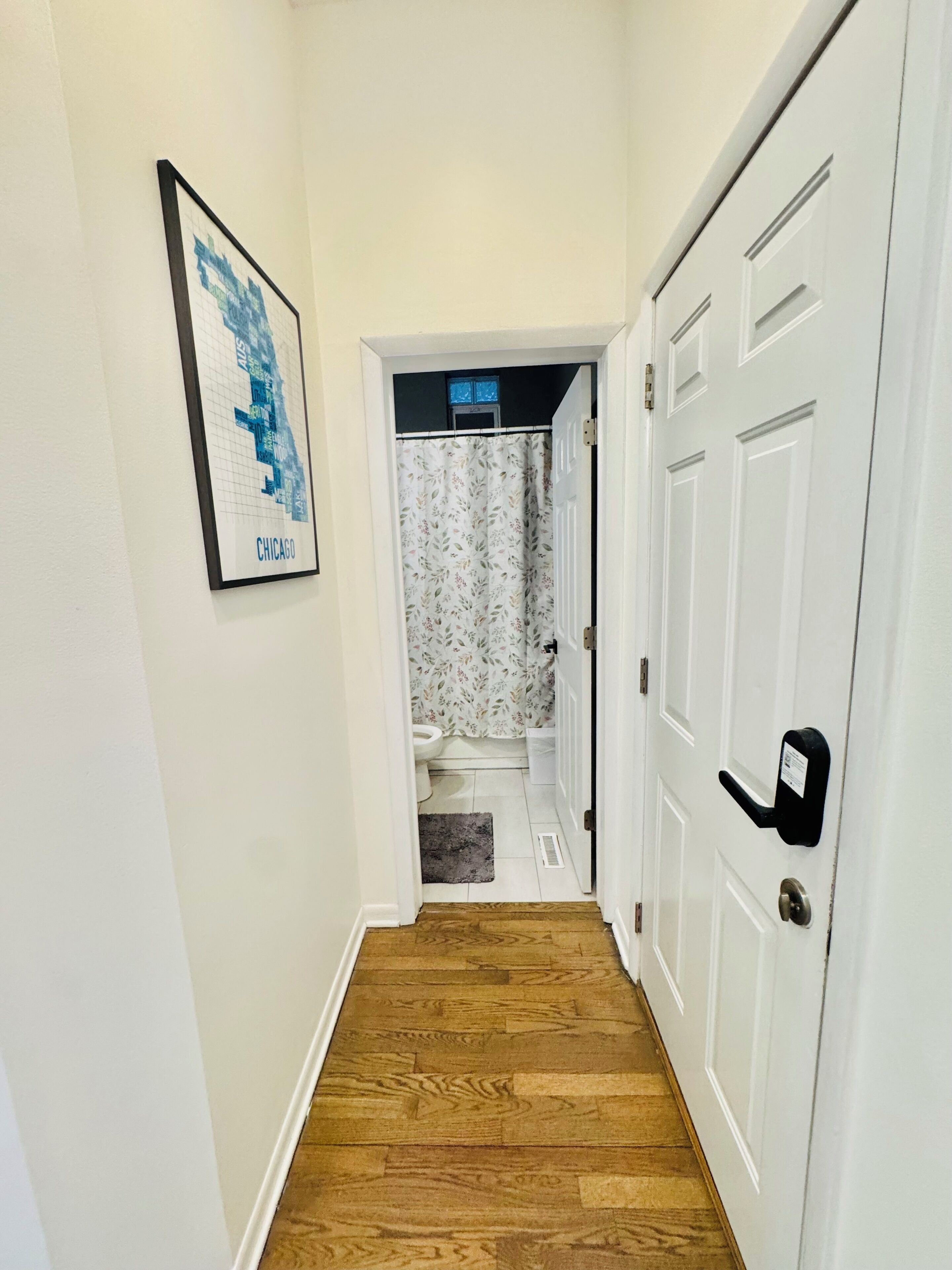 A hallway with a wooden floor, a white door with a black handle, and a framed map on the wall.