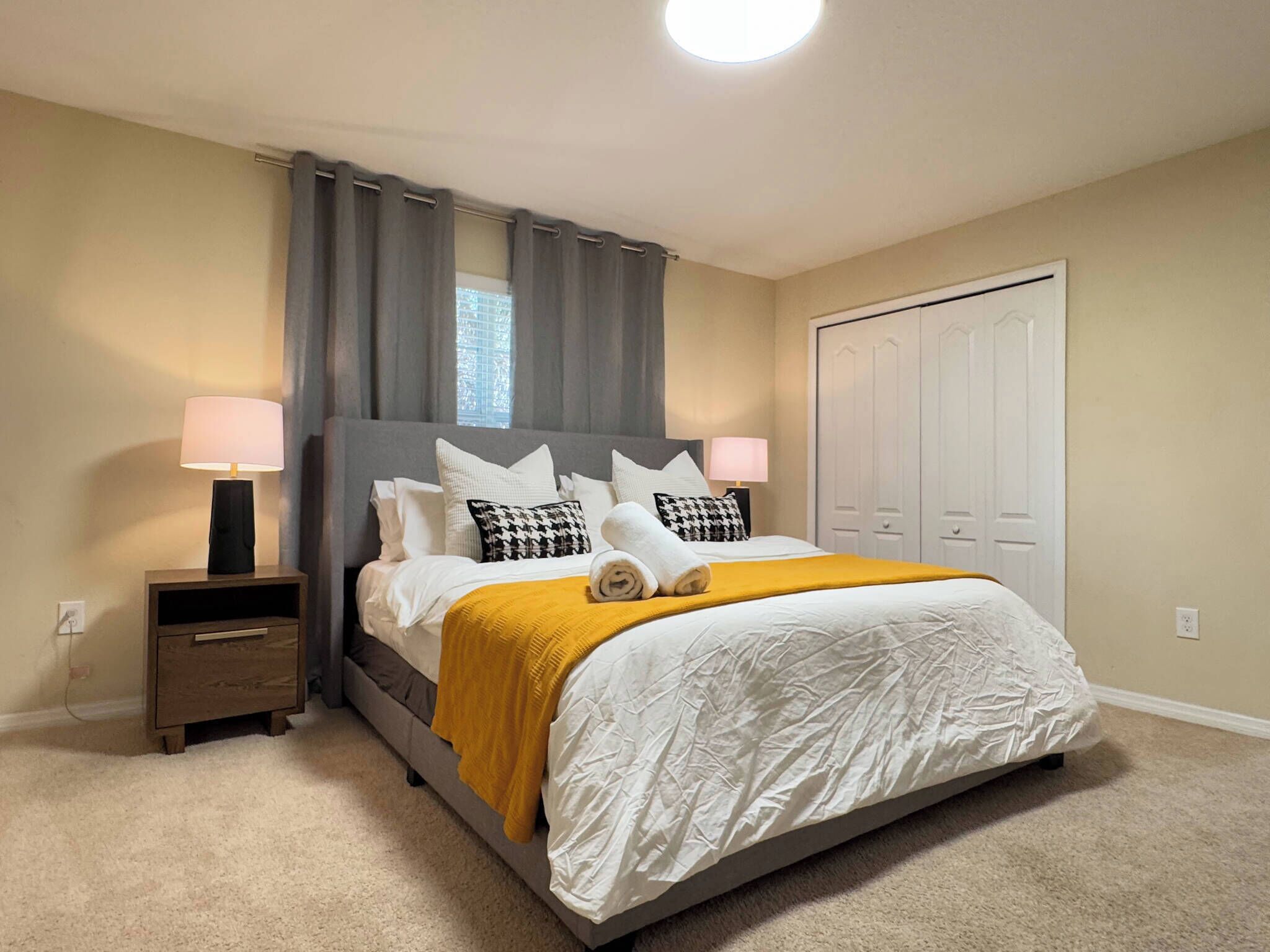 A bedroom with a bed, two bedside tables, a nightstand, a window with curtains, and a door.