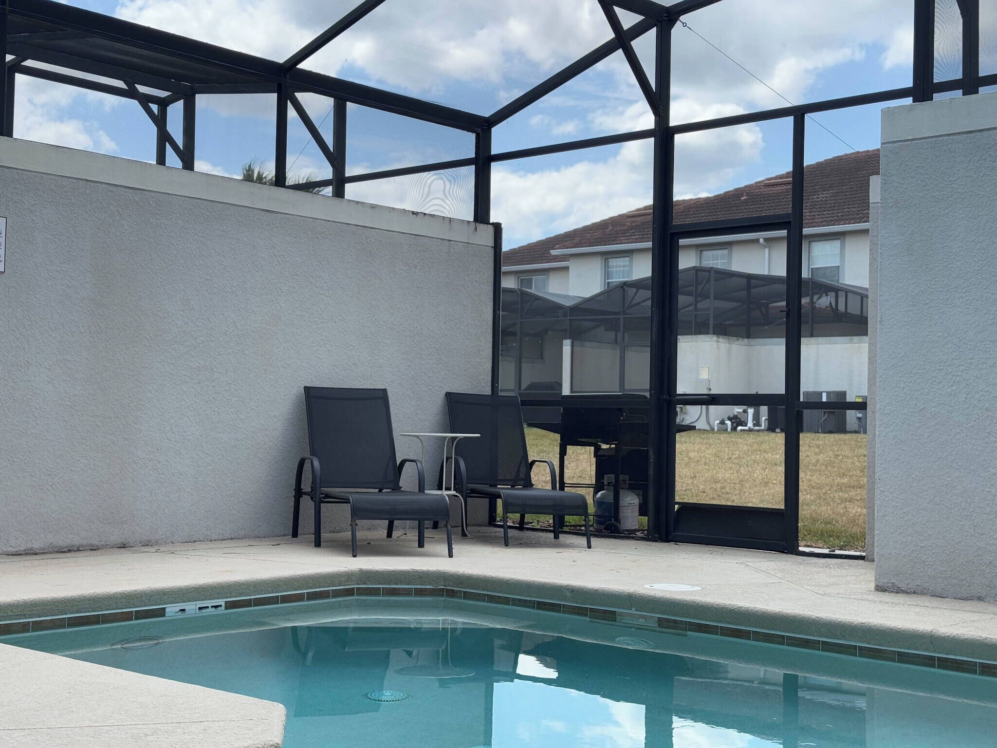Un espace piscine doté d’une structure en verre, de deux chaises longues et offrant une vue sur un immeuble d’habitation.