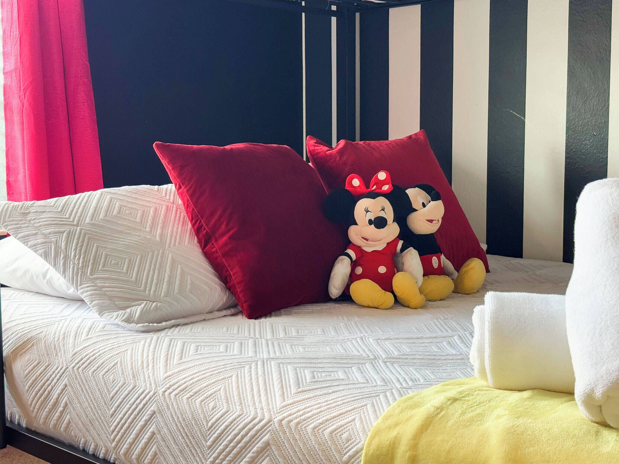 A bed with a patterned bedspread, red pillows, and two plush toys.