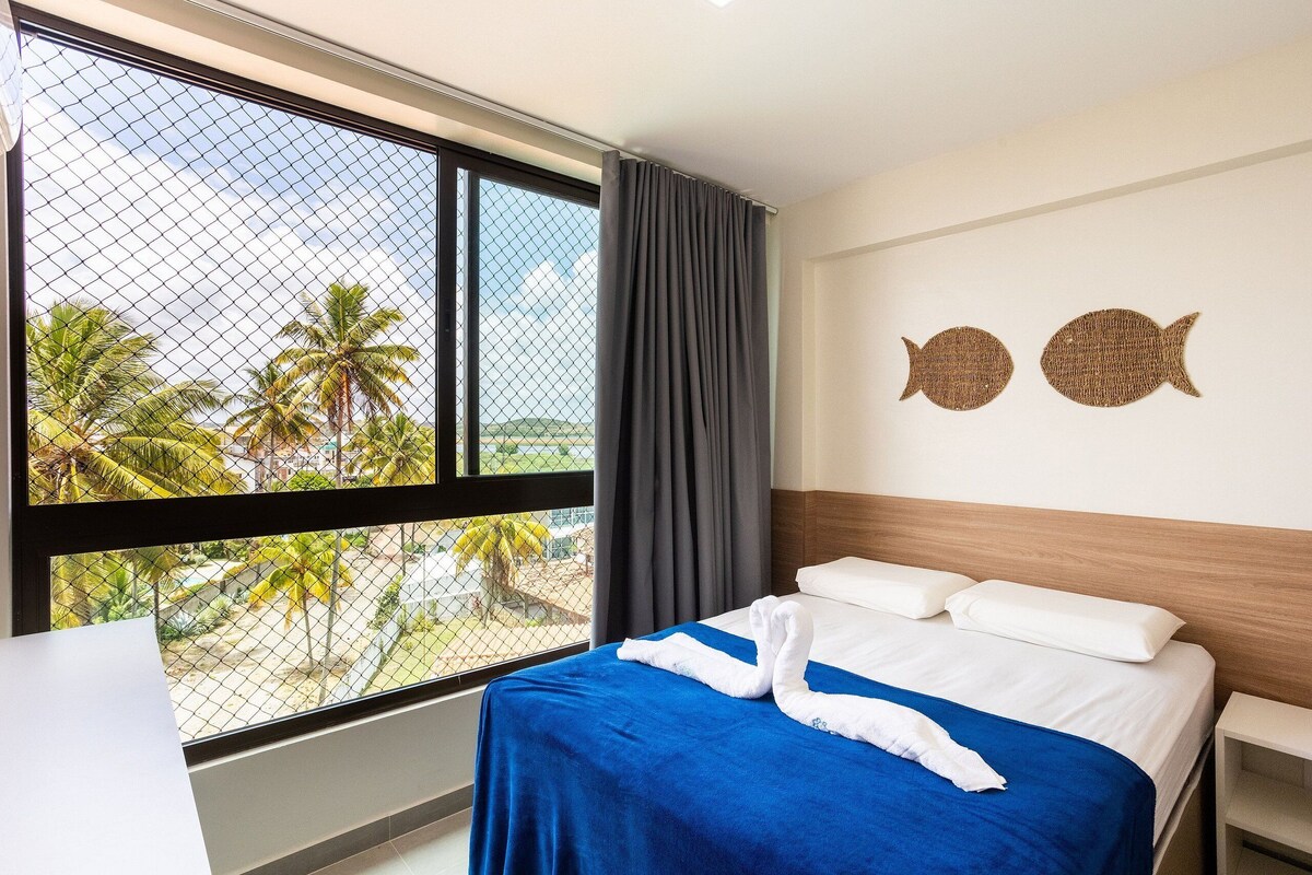 Ein Hotelzimmer mit großem Fenster, einem Bett mit weißer und blauer Bettwäsche sowie zwei an der Wand befestigten Fischornamenten.