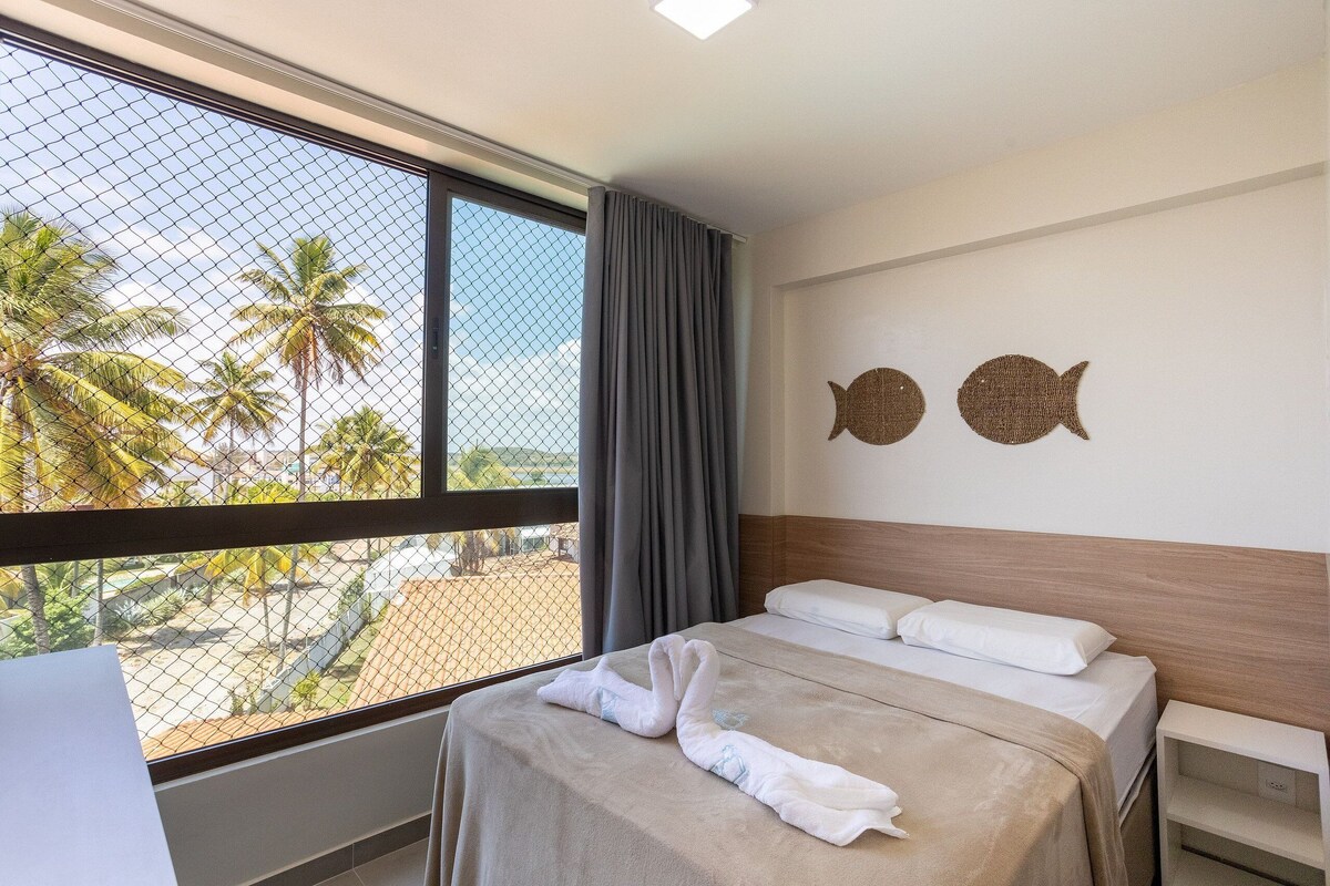 Ein Hotelzimmer mit einem Bett, einem Fenster mit Blick auf Palmen und zwei Wanddekorationen, die Fische darstellen.