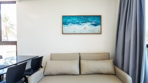 Et værelse med en beige sofa, to sorte stole, et bord og et billede af et blåt hav på væggen.