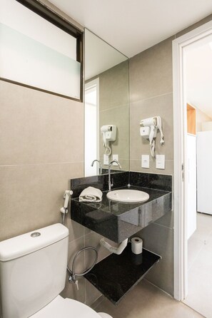 A modern bathroom with a toilet, sink, and hairdryer mounted on the wall. - Capri Residence (Ipojuca)