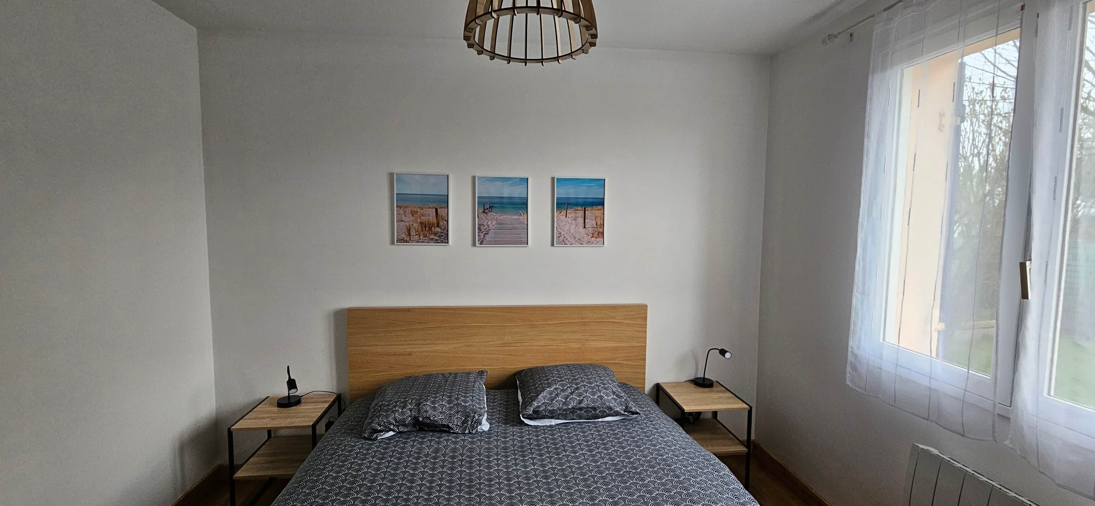 Ein Schlafzimmer mit Holzkopfteil, einem Bett mit gemusterten Betttextilien, zwei Nachttischen und drei gerahmten Bildern an der Wand.