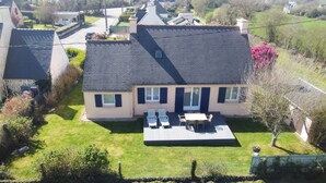 Uma casa de dois andares com telhado plano, um pátio com mesa e cadeiras, e um gramado bem cuidado.