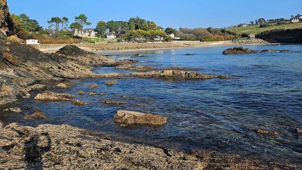 Paisagem costeira com costas rochosas, água cristalina e edifícios ao fundo.