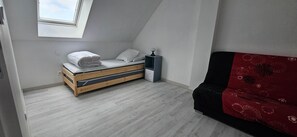 Une petite pièce avec un lit en mezzanine, une table de chevet, un canapé rouge et une lucarne.