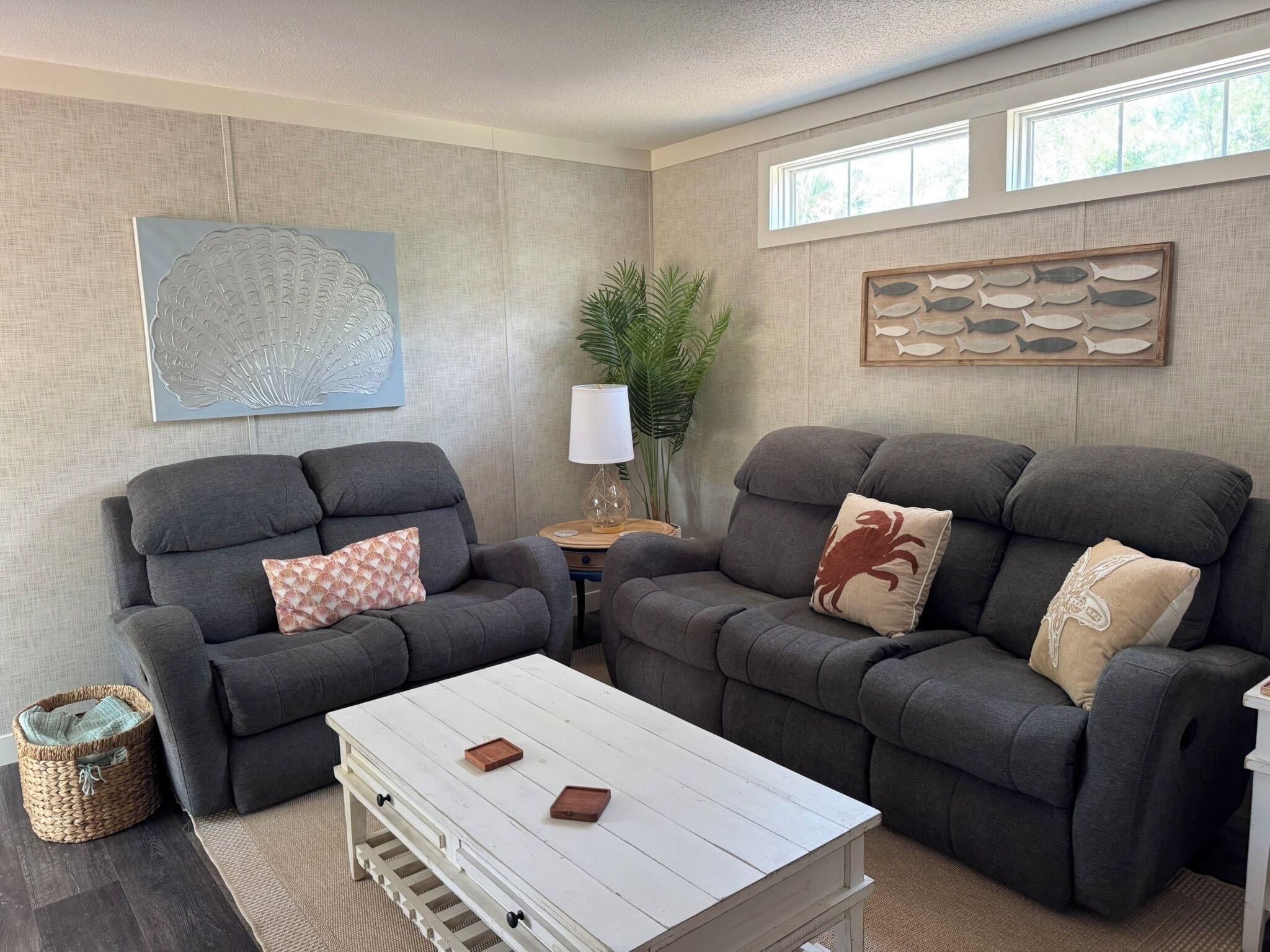 A living room with two grey sofas, a white coffee table, a woven basket, and wall art.